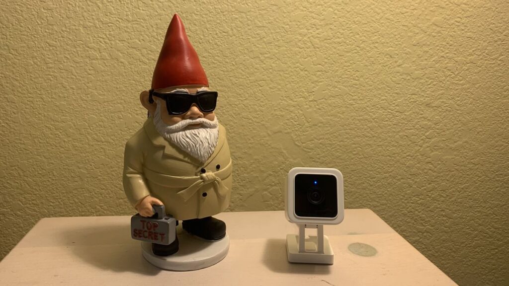 The Wyze Cam v3 next to a spy gnome with a briefcase that says